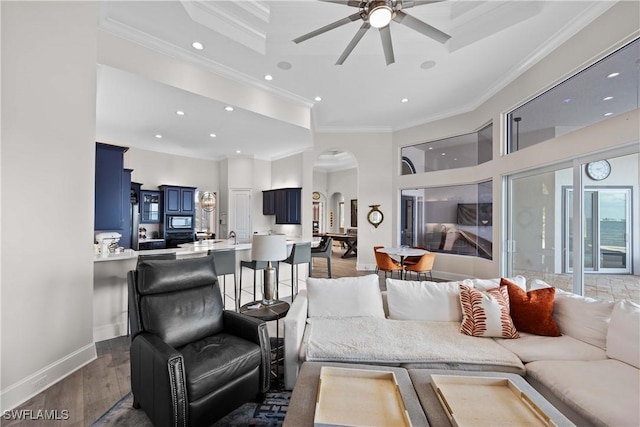 living room featuring arched walkways, recessed lighting, dark wood-type flooring, ornamental molding, and baseboards