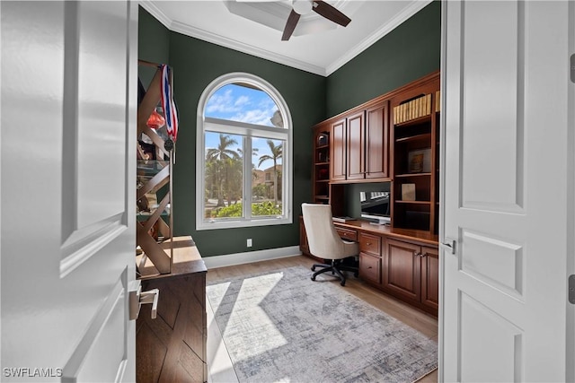 office featuring light wood-type flooring, baseboards, ornamental molding, and built in desk