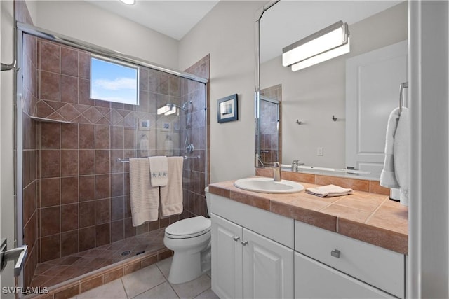 bathroom featuring toilet, tiled shower, vanity, and tile patterned floors