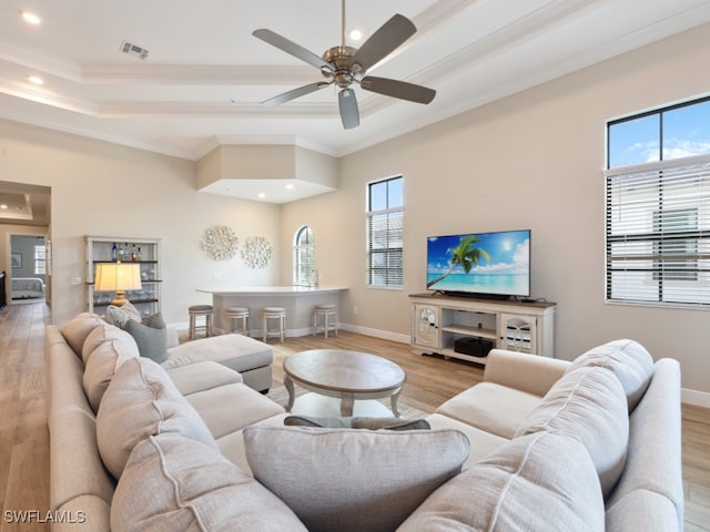 living room featuring light wood-type flooring, a raised ceiling, ceiling fan, and crown molding