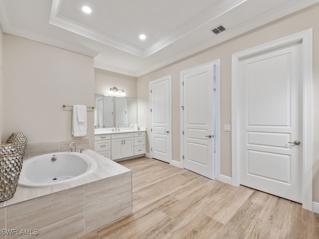 bathroom featuring ornamental molding, vanity, a raised ceiling, hardwood / wood-style floors, and tiled bath