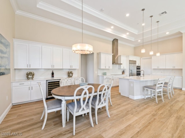 dining room featuring a raised ceiling, crown molding, beverage cooler, and light hardwood / wood-style flooring