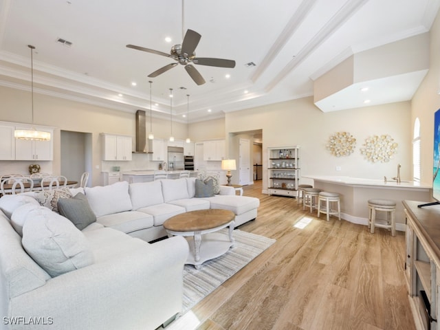 living room with ceiling fan, a raised ceiling, light hardwood / wood-style flooring, a towering ceiling, and ornamental molding