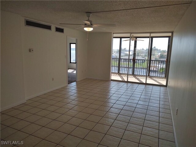 tiled empty room with a textured ceiling, a water view, and ceiling fan