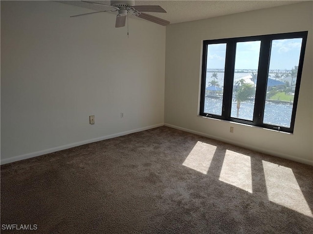 carpeted empty room with a textured ceiling, ceiling fan, a water view, and baseboards