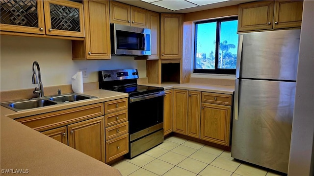 kitchen featuring light countertops, light tile patterned floors, a sink, appliances with stainless steel finishes, and brown cabinetry