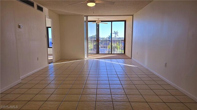 spare room with a wall of windows, light tile patterned floors, a textured ceiling, visible vents, and a ceiling fan
