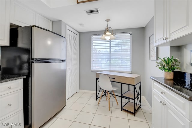 kitchen featuring stainless steel refrigerator, white cabinetry, dark stone countertops, light tile patterned floors, and hanging light fixtures