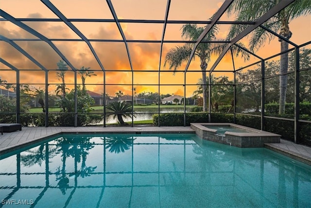 pool at dusk featuring a lanai, an in ground hot tub, and a water view