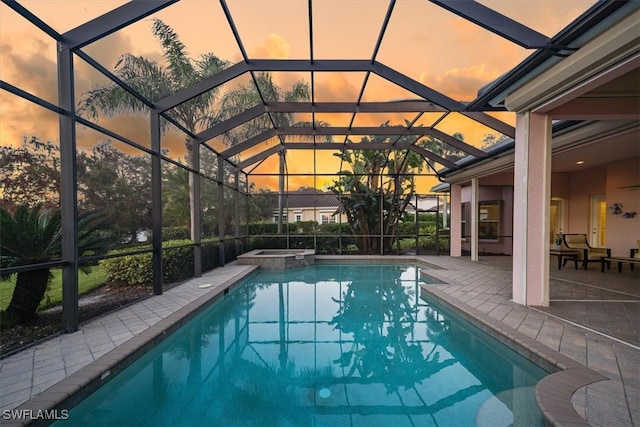 pool at dusk with an in ground hot tub, a patio area, and a lanai