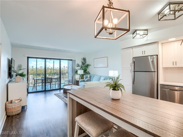 kitchen featuring white cabinets, open floor plan, wood finished floors, hanging light fixtures, and stainless steel appliances