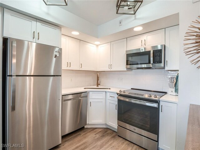 kitchen featuring stainless steel appliances, white cabinetry, sink, tasteful backsplash, and light hardwood / wood-style flooring