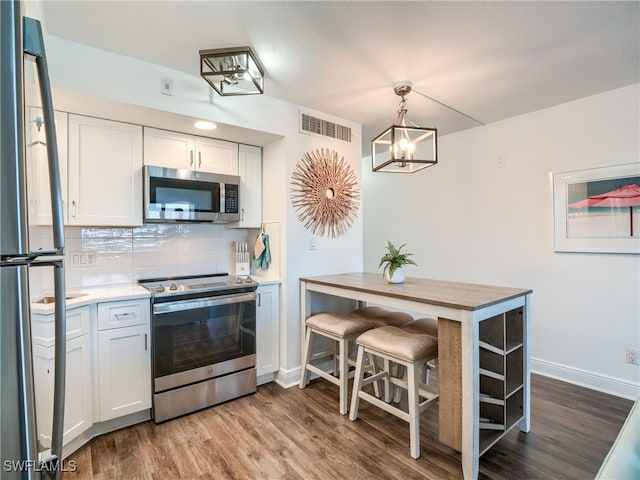 kitchen featuring white cabinetry, stainless steel appliances, decorative light fixtures, and backsplash