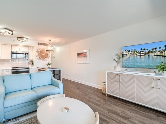 living area with an inviting chandelier, dark wood finished floors, visible vents, and baseboards