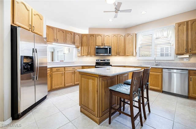 kitchen featuring a kitchen bar, appliances with stainless steel finishes, ceiling fan, light tile patterned floors, and a center island