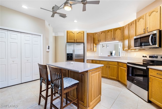 kitchen featuring a kitchen breakfast bar, stainless steel appliances, ceiling fan, a kitchen island, and light tile patterned flooring