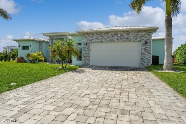 view of front of home featuring a front lawn, central AC unit, and a garage