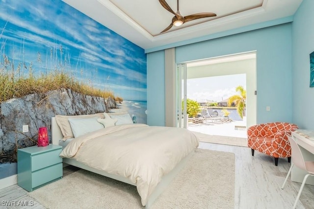 bedroom featuring access to outside, ceiling fan, hardwood / wood-style floors, and a tray ceiling