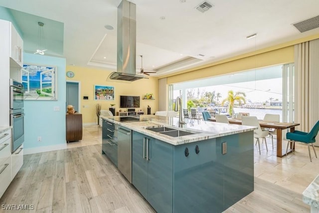 kitchen with a raised ceiling, sink, ceiling fan, light wood-type flooring, and island exhaust hood