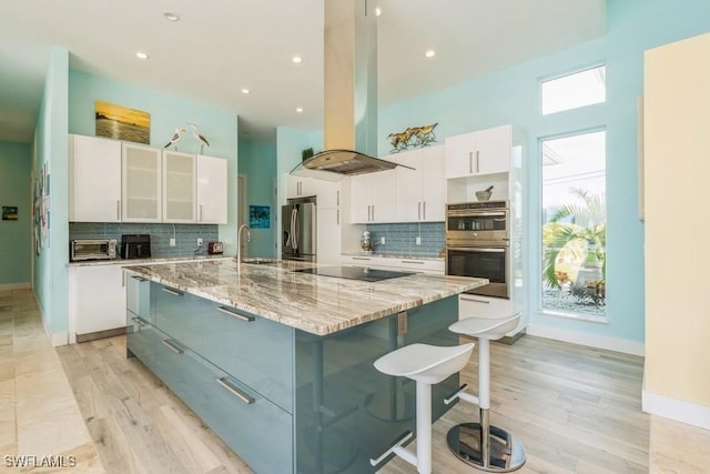 kitchen with white cabinets, light hardwood / wood-style flooring, appliances with stainless steel finishes, a large island, and island exhaust hood