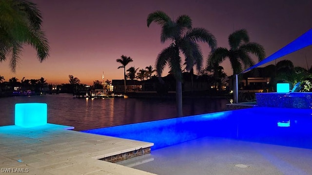 pool at dusk featuring pool water feature