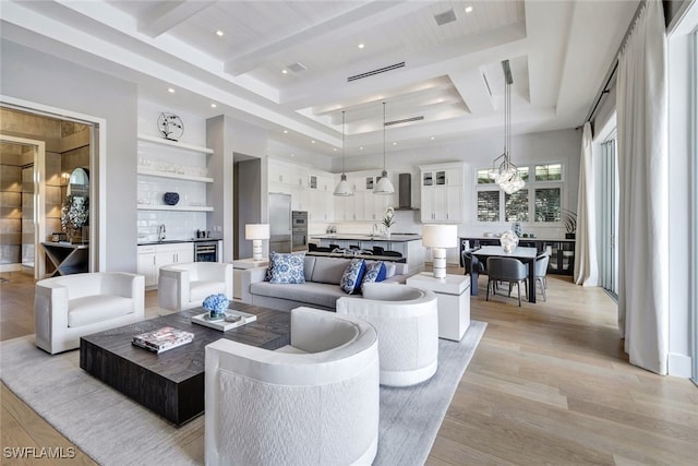 living room featuring sink, an inviting chandelier, a raised ceiling, light hardwood / wood-style flooring, and beamed ceiling