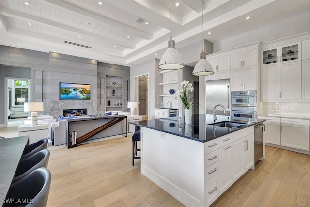 kitchen with a center island with sink, sink, a premium fireplace, beamed ceiling, and white cabinetry