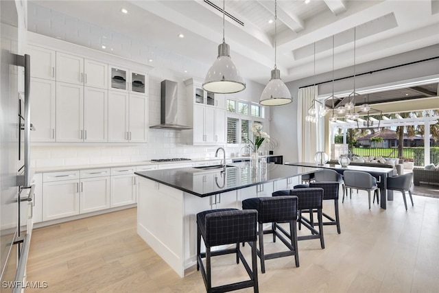 kitchen featuring white cabinetry, an island with sink, light hardwood / wood-style floors, and wall chimney range hood