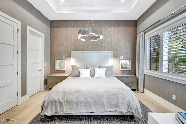 bedroom featuring a chandelier, light wood-type flooring, and a tray ceiling