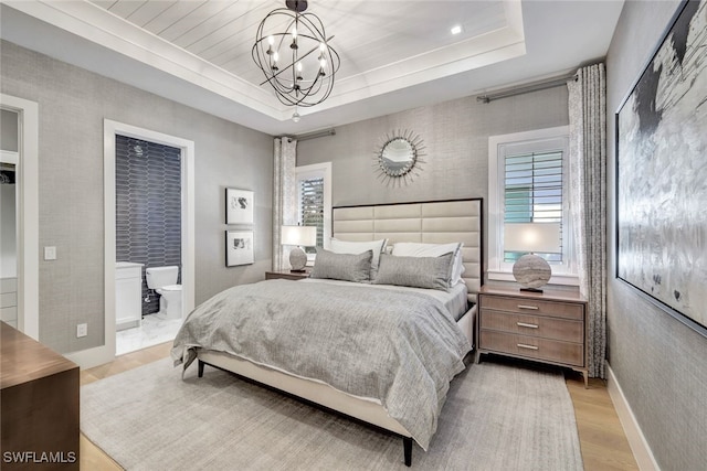 bedroom with a notable chandelier, ensuite bathroom, a raised ceiling, and light hardwood / wood-style flooring