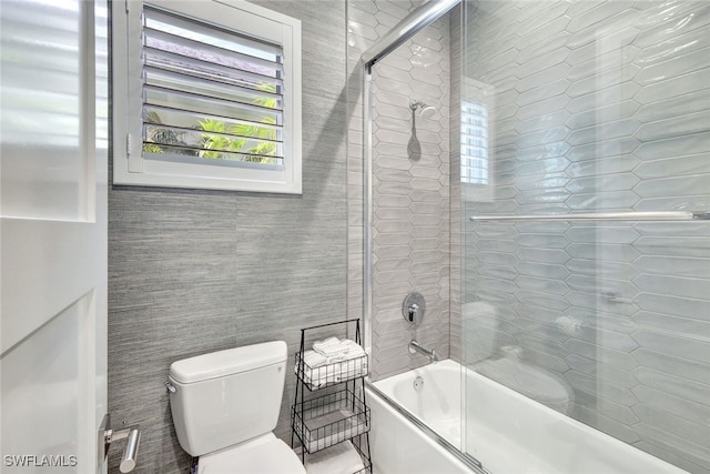 bathroom with enclosed tub / shower combo, tile walls, and toilet