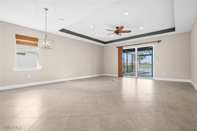 unfurnished room featuring a tray ceiling, light tile patterned flooring, and ceiling fan with notable chandelier