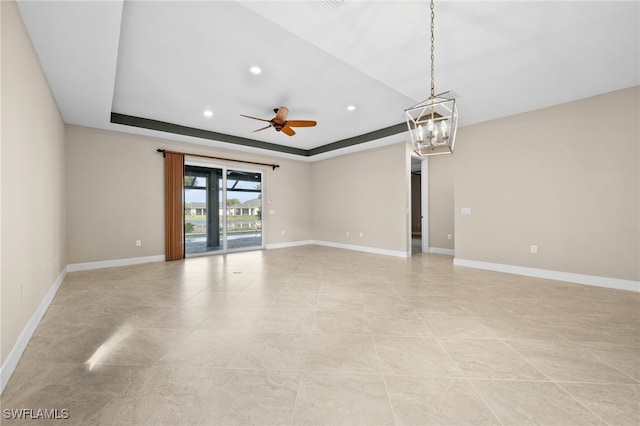 spare room with ceiling fan with notable chandelier and a tray ceiling