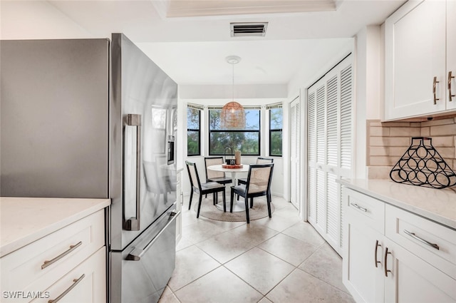 kitchen with light tile patterned flooring, stainless steel refrigerator with ice dispenser, hanging light fixtures, white cabinets, and decorative backsplash