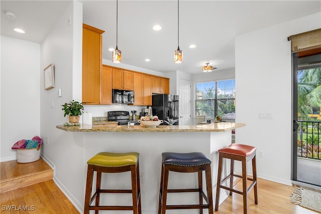 kitchen with light hardwood / wood-style floors, light stone counters, kitchen peninsula, black appliances, and decorative light fixtures