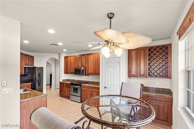 kitchen with sink, appliances with stainless steel finishes, dark stone counters, ceiling fan, and light tile patterned floors