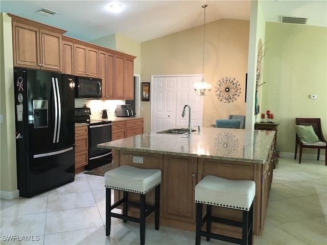 kitchen with a kitchen bar, vaulted ceiling, black appliances, sink, and an island with sink