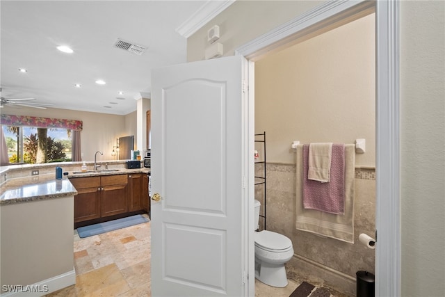 bathroom featuring toilet, tile walls, vanity, ceiling fan, and crown molding