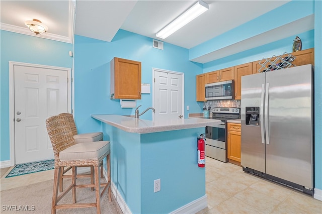 kitchen with light tile patterned flooring, crown molding, stainless steel appliances, a breakfast bar area, and kitchen peninsula