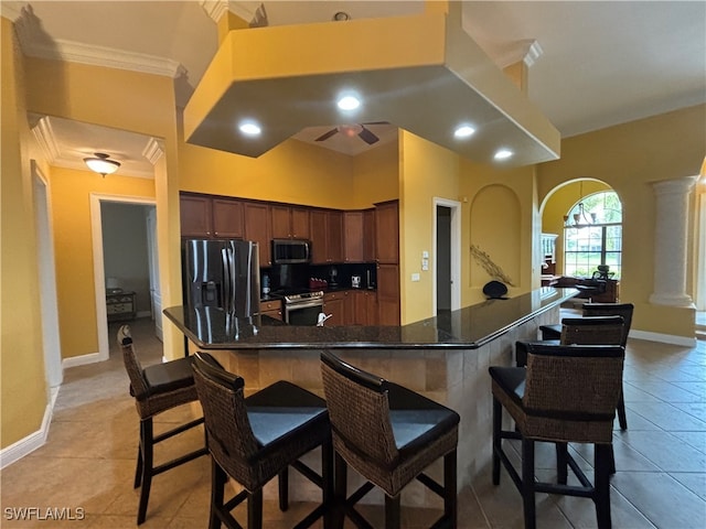 kitchen with appliances with stainless steel finishes, light tile patterned floors, crown molding, and a breakfast bar