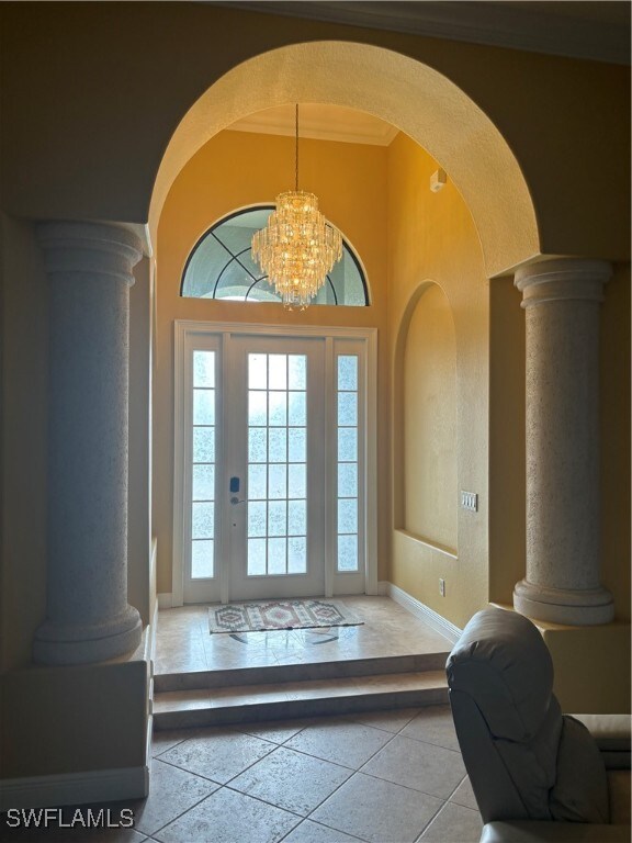 tiled foyer featuring a chandelier and crown molding