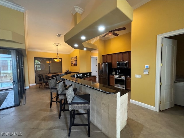 kitchen featuring stainless steel appliances, kitchen peninsula, a breakfast bar area, decorative light fixtures, and crown molding