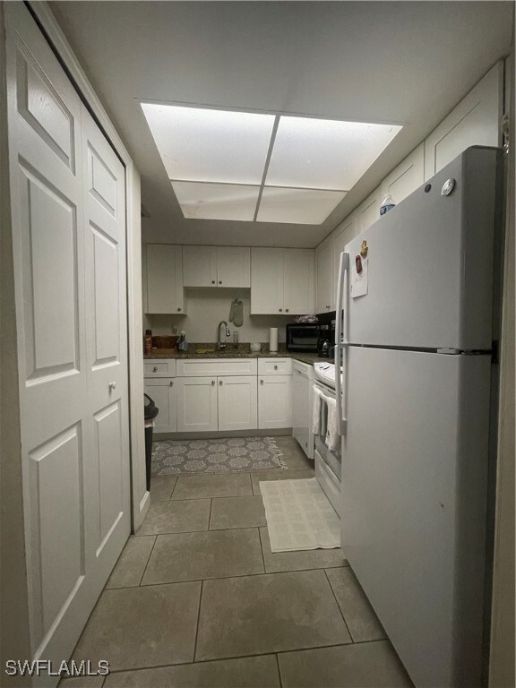 kitchen featuring white cabinets, sink, light tile patterned floors, and white appliances