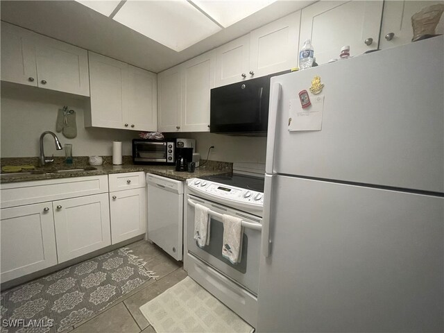 kitchen with dark stone countertops, sink, light tile patterned floors, white cabinets, and white appliances