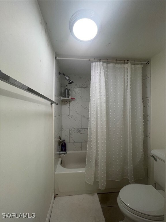 bathroom featuring toilet, shower / bath combo with shower curtain, and tile patterned flooring