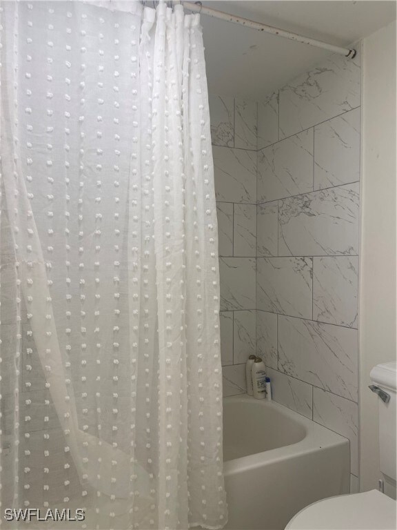 bathroom with shower / bath combination with curtain and toilet