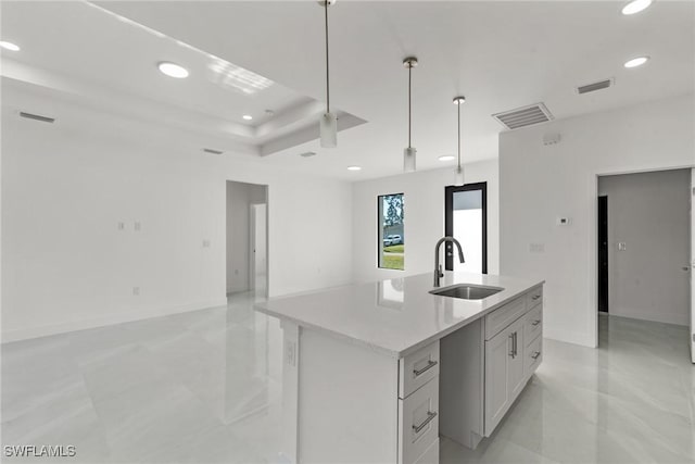 kitchen featuring white cabinets, sink, an island with sink, and hanging light fixtures