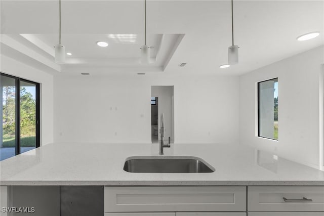 kitchen featuring a raised ceiling, decorative light fixtures, light stone counters, and sink