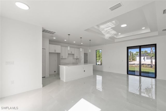 kitchen featuring a wealth of natural light, a center island with sink, white cabinets, and hanging light fixtures