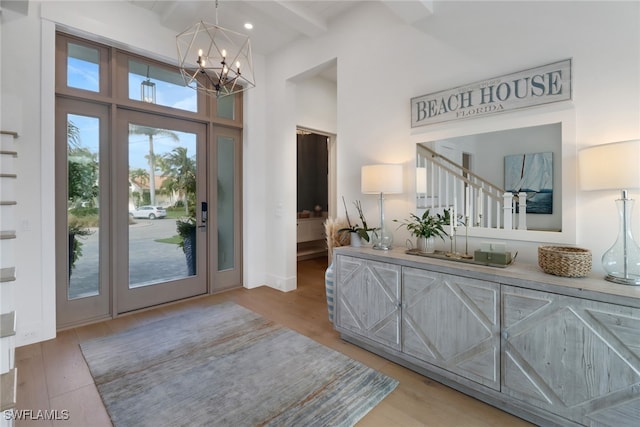 foyer entrance featuring a towering ceiling, beamed ceiling, an inviting chandelier, and light wood-type flooring